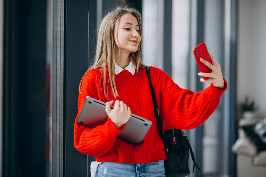 girl student holding computer and talking on the phone by the window