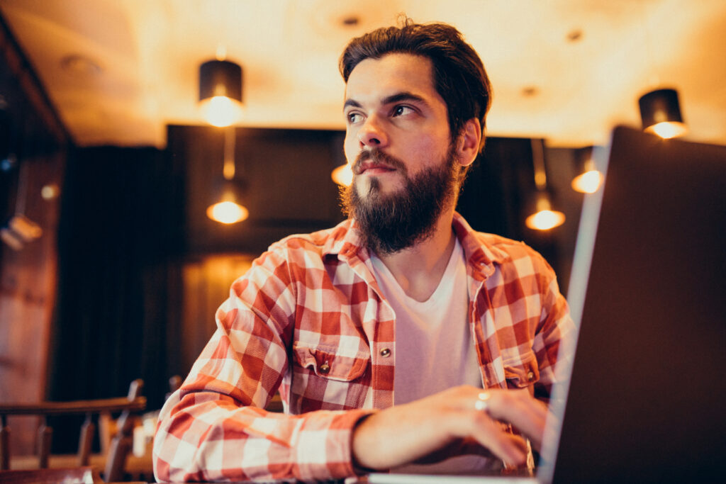youn g bearded man working on laptop in a bar